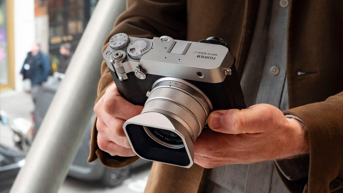 Cầm máy ảnh Fujifilm GFX100RF góc cận cảnh ngoài trời với phông nền đường phố