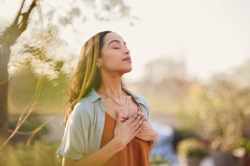 Young latin woman with hand on chest breathing in fresh air in a beautiful garden during sunset. Hea.jpg