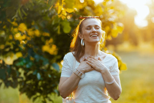 Summer time. smiling modern woman in white shirt with hand on chest outside in nature..jpg