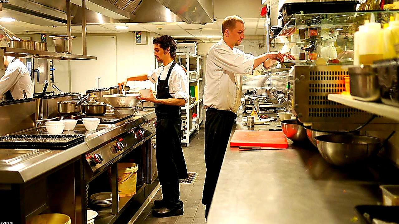 Bright colorful hero photo of a modern restaurant kitchen pass with chefs plating vibrant dishes under warm lights