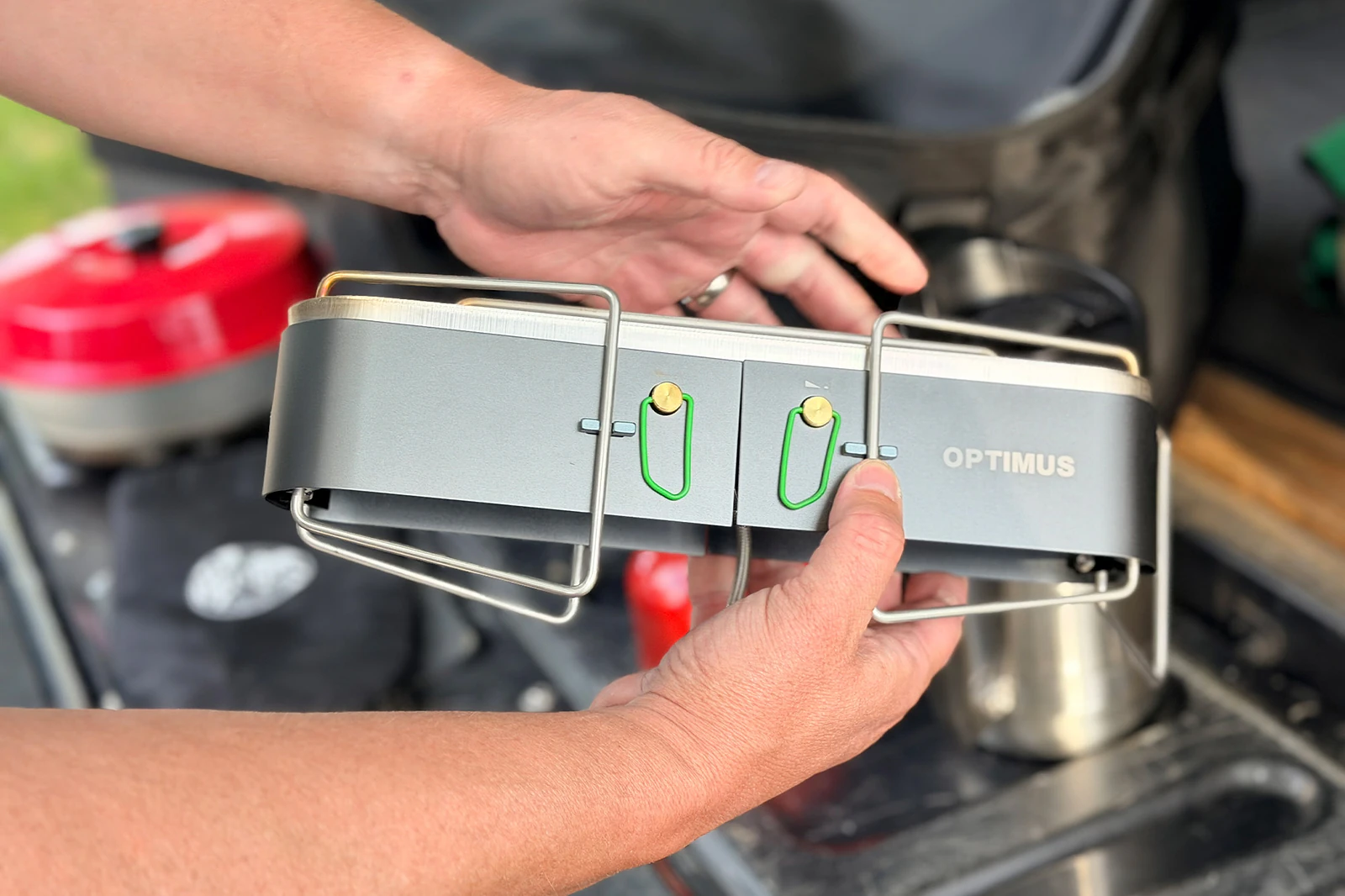 Hands holding the folded Optimus Gemini II stove