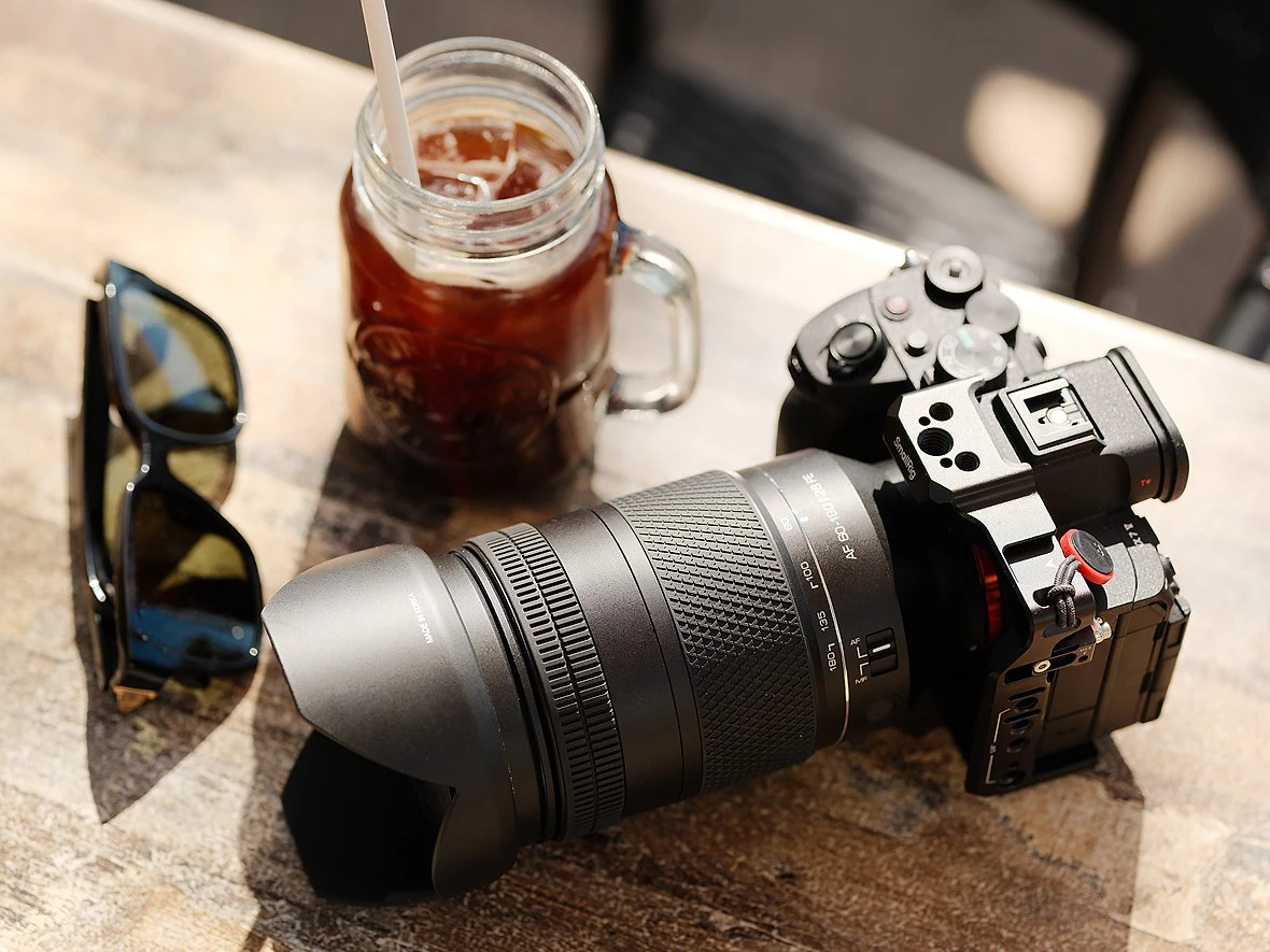 a camera sits on a wood table next to a coffee and sunglasses