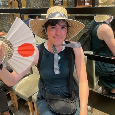 Portrait of Rose Traviss wearing a sun hat and holding a fan
