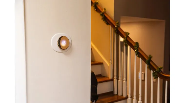The fourth-gen Google Nest learning thermostat hung up on a wall near a staircase.