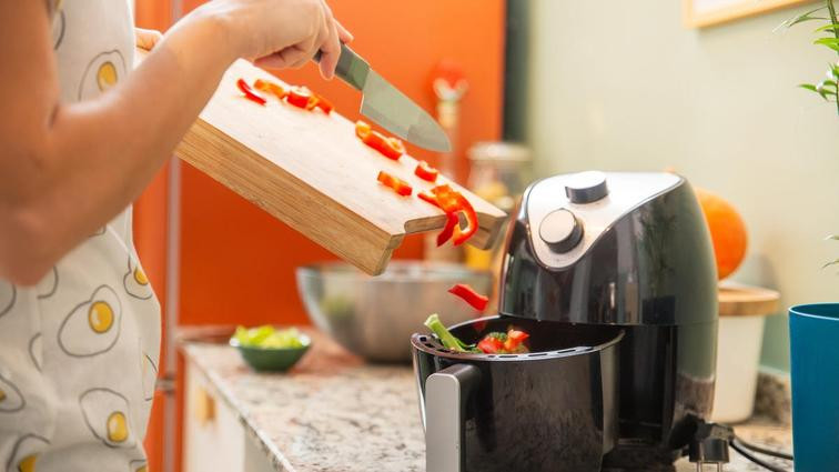 person scraping chopped veggies into air fryer