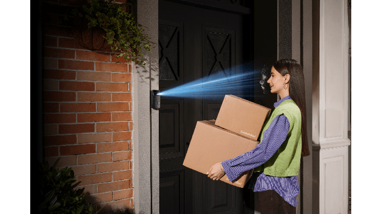 None A woman holding packages approaches a front door where a keypad is scanning her face.