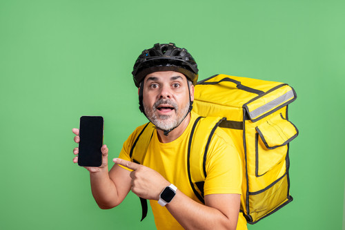 delivery man showing smartphone with surprised look green screen background yellow outfit.jpg