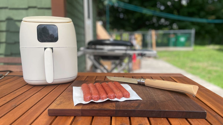 None air fryer and hot dogs sit on a cutting board out on a patio table in summer