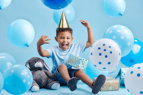 Excited little boy celebrating his birthday with balloons and gifts on a blue studio background. Cut.jpg