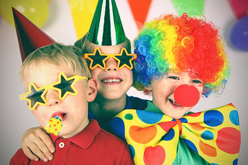 Three boys dressed up in colorful party clothing are celebrating a birthday. One child is wearing a .jpg