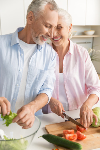Image of happy mature loving couple family standing at the kitchen and cooking salad. Looking aside..jpg