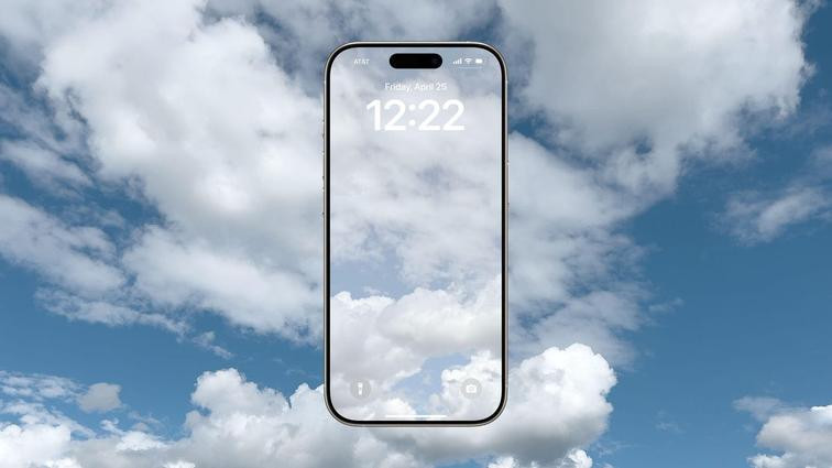 None An iPhone with a cloud image wallpaper floating in front of a sky full of clouds.