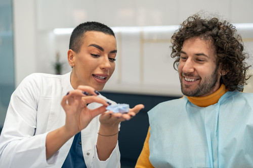 young confident attractive woman dentist smiling handsome young man patient looking dental model imp.jpg