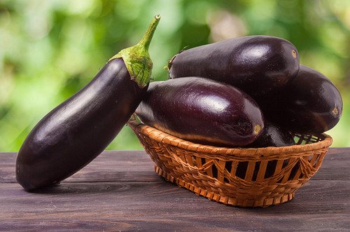 eggplant in a wicker basket on wooden table with blurred green background.jpg