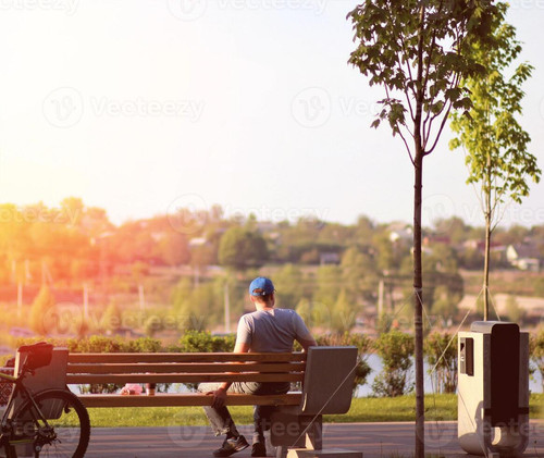 lonely young man sitting on a bench in the park near the lake on sunset coffee break photo.jpg