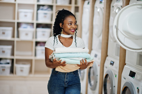 cheerful african american woman with towels hands near washing machine selfservice laundry.jpg