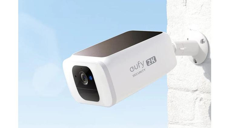 None The Eufy SoloCam S230 mounted to a white brick wall against blue sky.