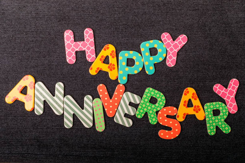 Card with Happy Anniversary words made from mixed vivid colored wooden letters on a textured dark bl.jpg