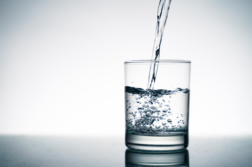 Close up of pouring fresh water into the clear glass from the bottle on table..jpg
