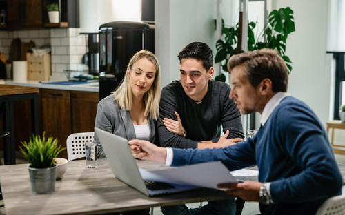 young couple real estate agent using laptop while going through housing plan meeting min.jpg