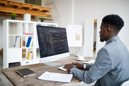 Young elegant software developer in formalwear sitting by desk in front of computer screen while dec.jpg