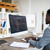 Young elegant software developer in formalwear sitting by desk in front of computer screen while dec