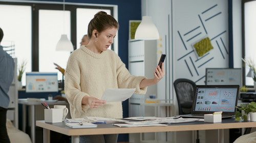 Woman using smartphone in video call conference talking about sales holding paper with charts in bus.jpg