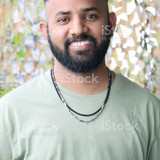 Stock photo showing headshot of Indian man with shaved head wearing t-shirt and necklaces.