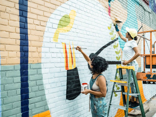 Two Female artists painting large wall mural. They are dressed in casual work clothes. Exterior of p.jpg