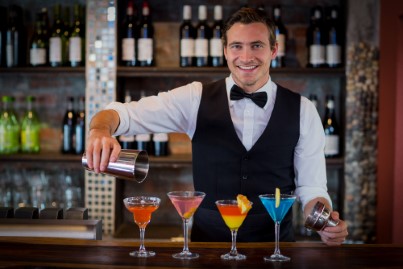 Portrait of bartender pouring a orange martini drink in the glass at bar.jpg