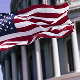The flag of the united states of america flying in front of the capitol building blurred in the back