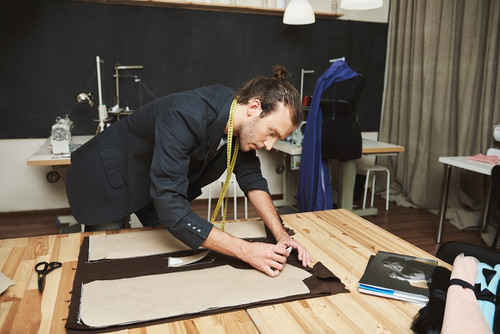 Portrait of serious young good-looking hispanic fashion designer in black suit cutting out parts of .jpg