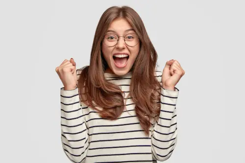 glad european woman wears spectacles clenches fists excitement wears round spectacles casual sweater.webp