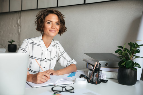 Smiling pretty woman working by the table in co working office and looking at the camera.jpg