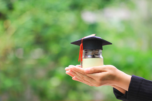 Woman hand holding coins money in glass bottle with graduates hat on natural green background, Savin.jpg