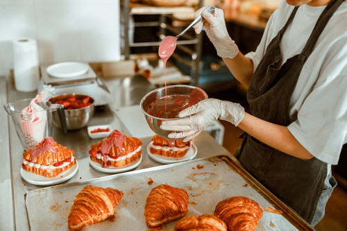 Woman holds spoon with pouring down frosting above bowl at metal table with tasty croissants in craf.jpg