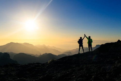 Couple hikers celebrating success in sunset mountains, accomplish with arms up outstretched. Young m.jpg