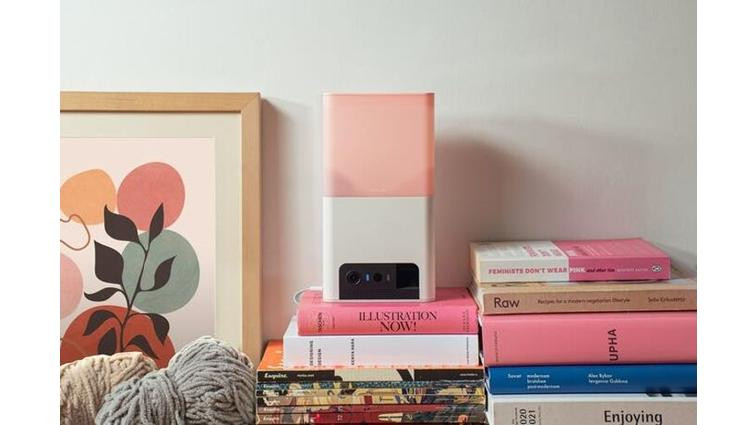 None A Petcube Bites 2 Lite sits on top of books amid cozy decor.