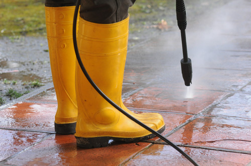 person wearing yellow rubber boots with high pressure water nozzle cleaning dirt tiles.jpg