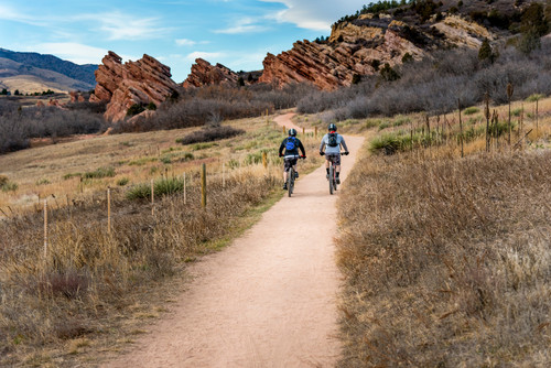Two cyclists ride mountain bikes side by side up a beautiful, dirt bike trail leading to red rocks o.jpg