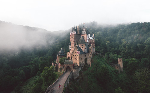 a castle on a hill with fog with Eltz Castle in the background.jpg
