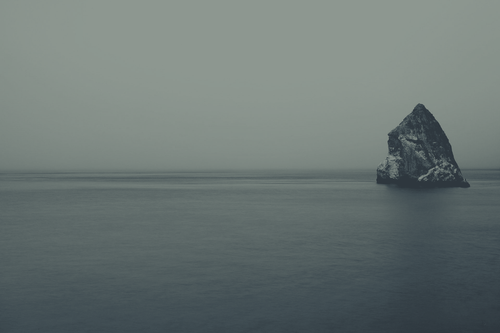 a large rock in the middle of a body of water.png