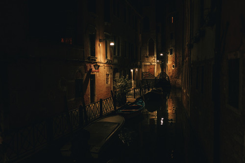 a narrow canal with boats and buildings at night.jpg