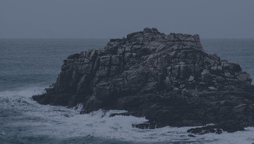 a rocky island with waves crashing on it.png