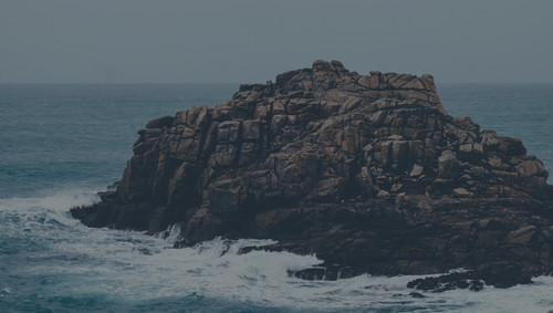 a rocky island with waves crashing on it.jpg