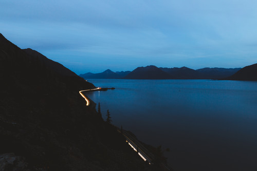 a road with lights on the side of a body of water.jpg