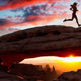 Young female runner running over Mesa Arch rock formation at sunset, Moab, Utah, USA1080p