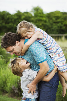 a father and two children in a garden a boy hugging him around the waist and a girl on his back with.jpg