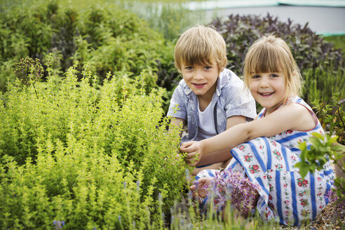 boy and girl kneeling side by side by a shrub in a garden smiling at camera MINF04418.jpg
