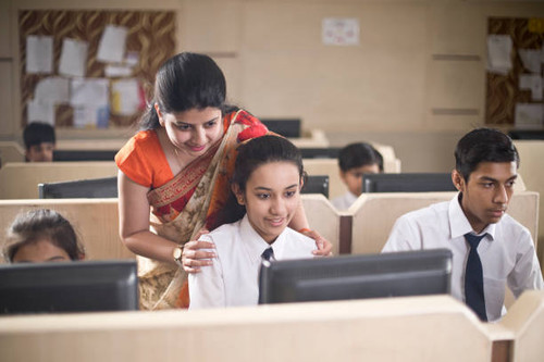 Teacher assisting a school girl in computer class.jpg